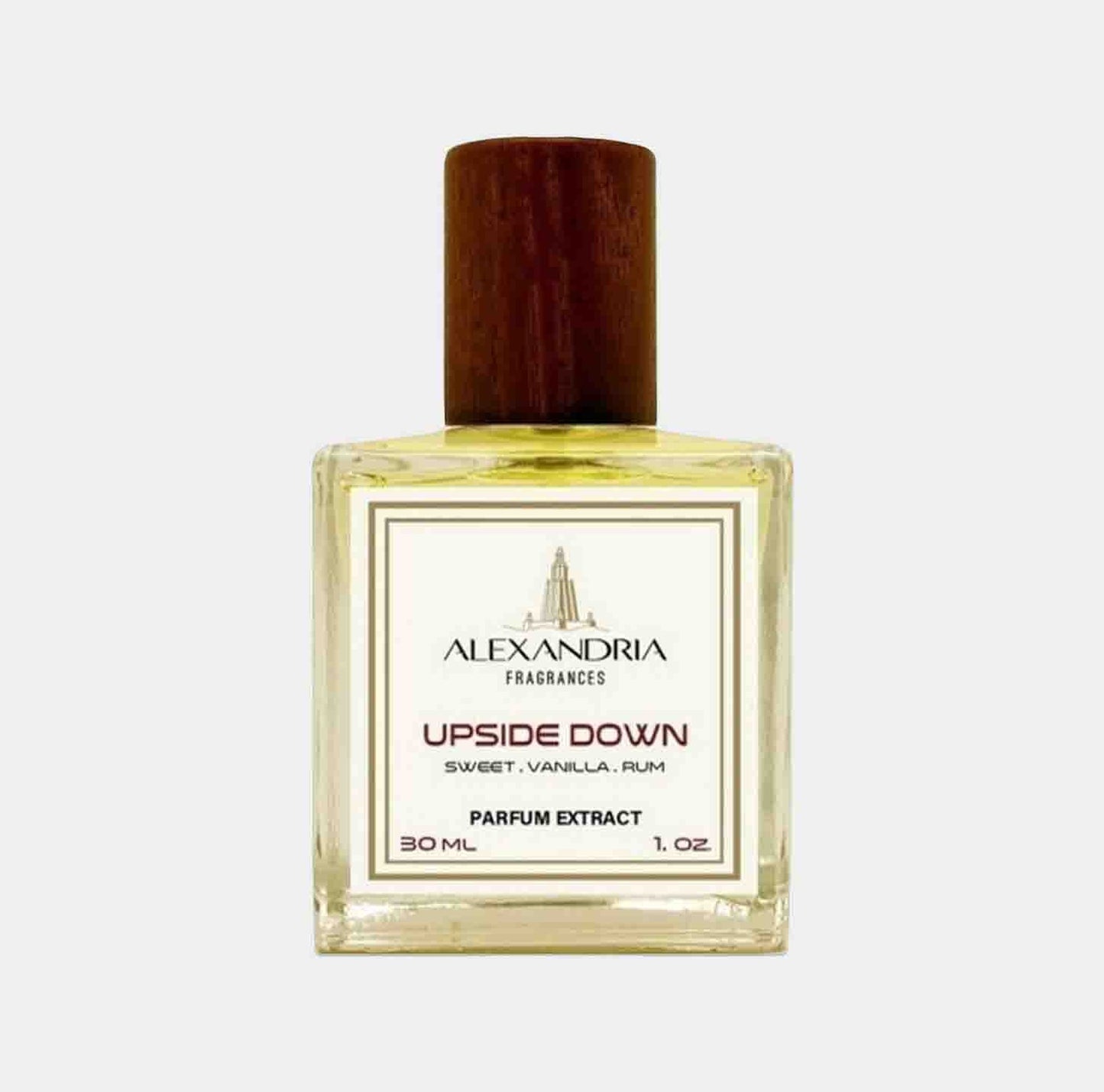 A bottle of Alexandria Fragrances Upside Down Sample, featuring a sleek glass container with a wooden cap, filled with a golden liquid. The label indicates it is a parfum extract with sweet notes of vanilla and rum, and holds 30 ml (1 oz).