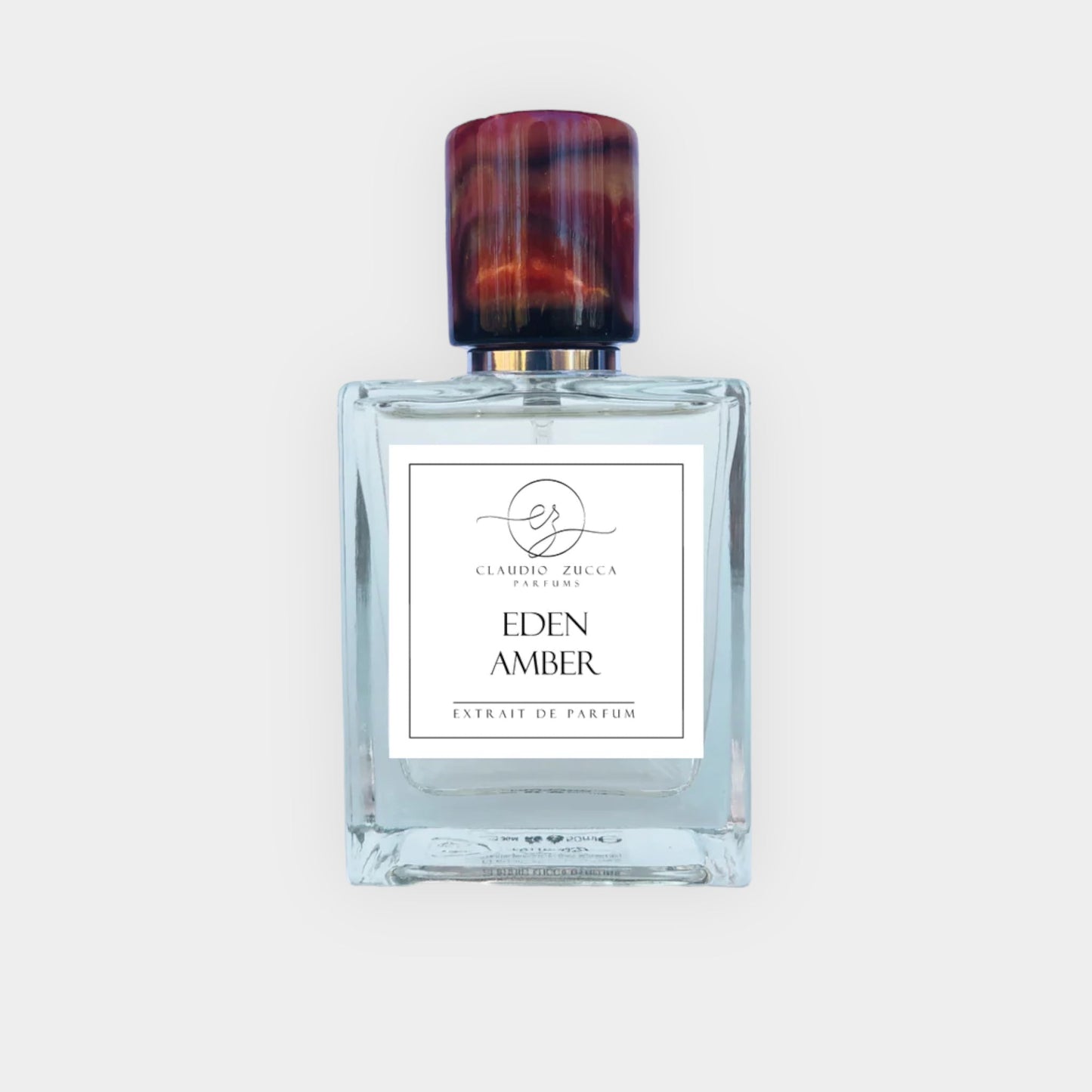 A full bottle of Claudio Zucca Eden Amber parfum, featuring an elegantly designed glass bottle with a sculpted amber-colored cap and a simple label that reads EDEN AMBER Extrait de Parfum.