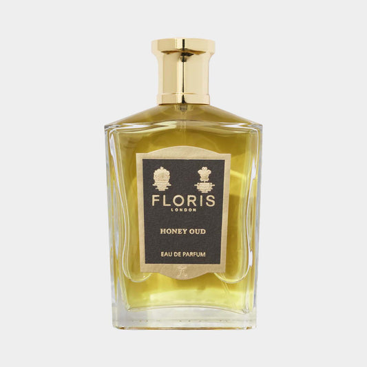 A clear glass bottle of Floris London Honey Oud perfume, featuring a gold cap and a black and gold label, showcasing its luxurious scent with hints of honey and oud.