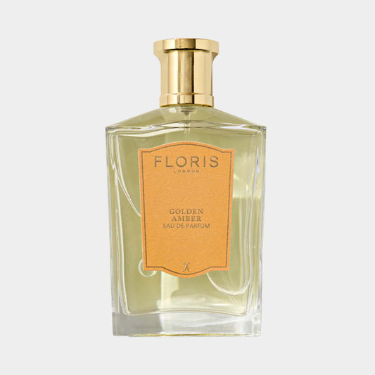 A clear glass bottle of Floris London Golden Amber Eau de Parfum, featuring an elegant gold cap and a warm amber-hued liquid, with a simple orange label indicating the fragrance.