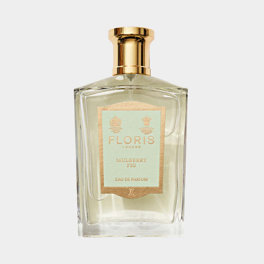 A clear glass bottle of Floris London Mulberry Fig Eau de Parfum, featuring a gold cap and a decorative label with a light blue and gold design. The fragrance encapsulates a blend of mulberry and fig notes.