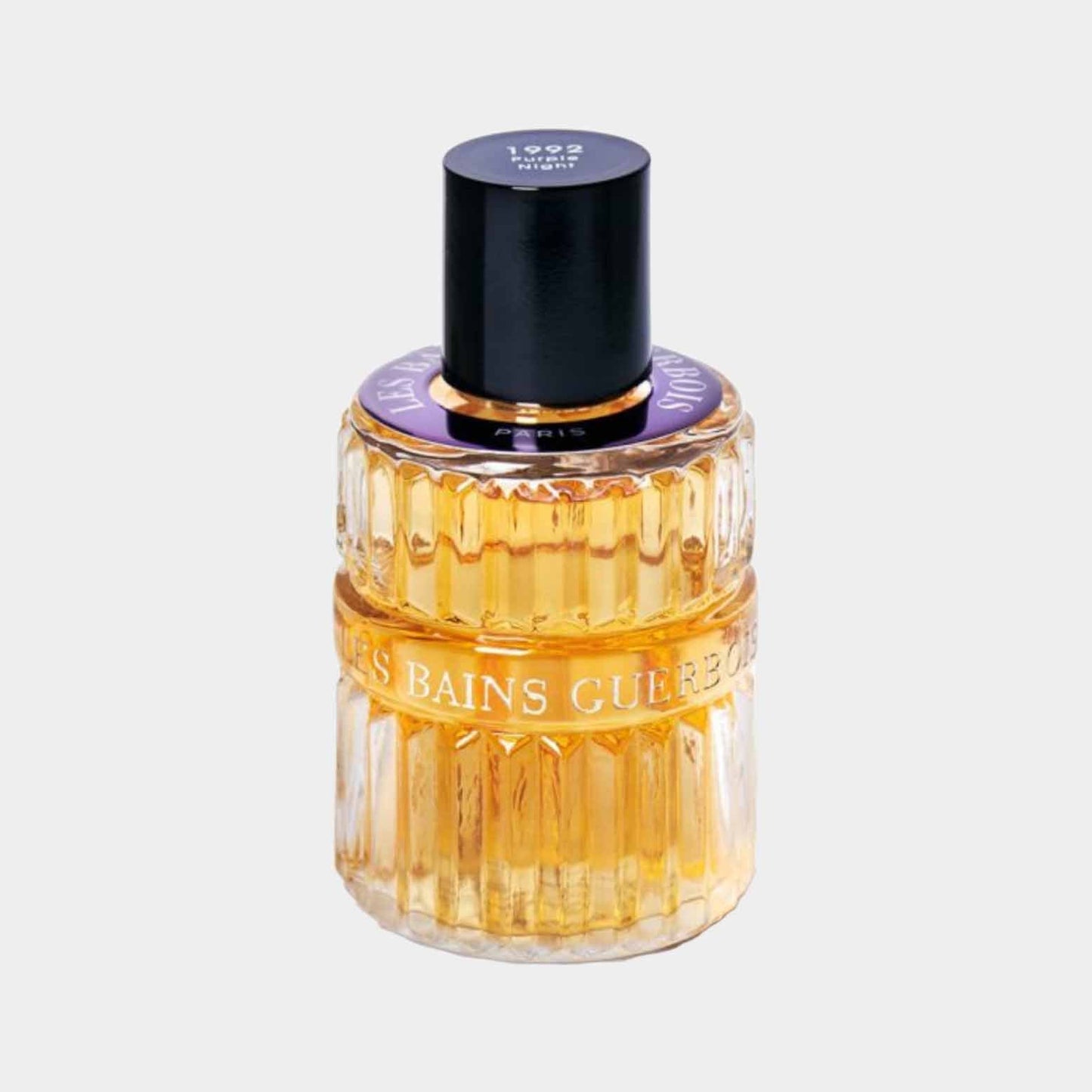 A full bottle of Les Bains Guerbois Purple Night 1992 perfume, featuring a ribbed glass design with a gold-hued liquid and a black cap.