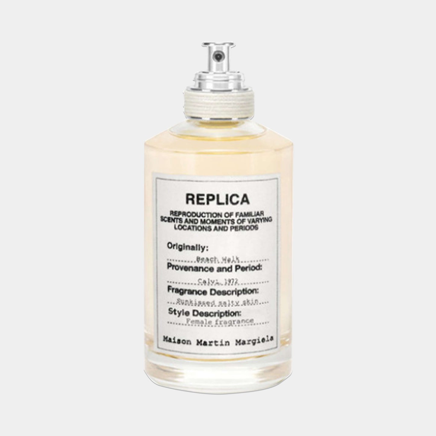 A bottle of Maison Martin Margiela Replica Beach Walk Sample perfume, featuring a clear glass design with a silver cap and a label detailing its fragrance description and origins. The liquid inside has a light yellow hue, evoking a sunny beach atmosphere.