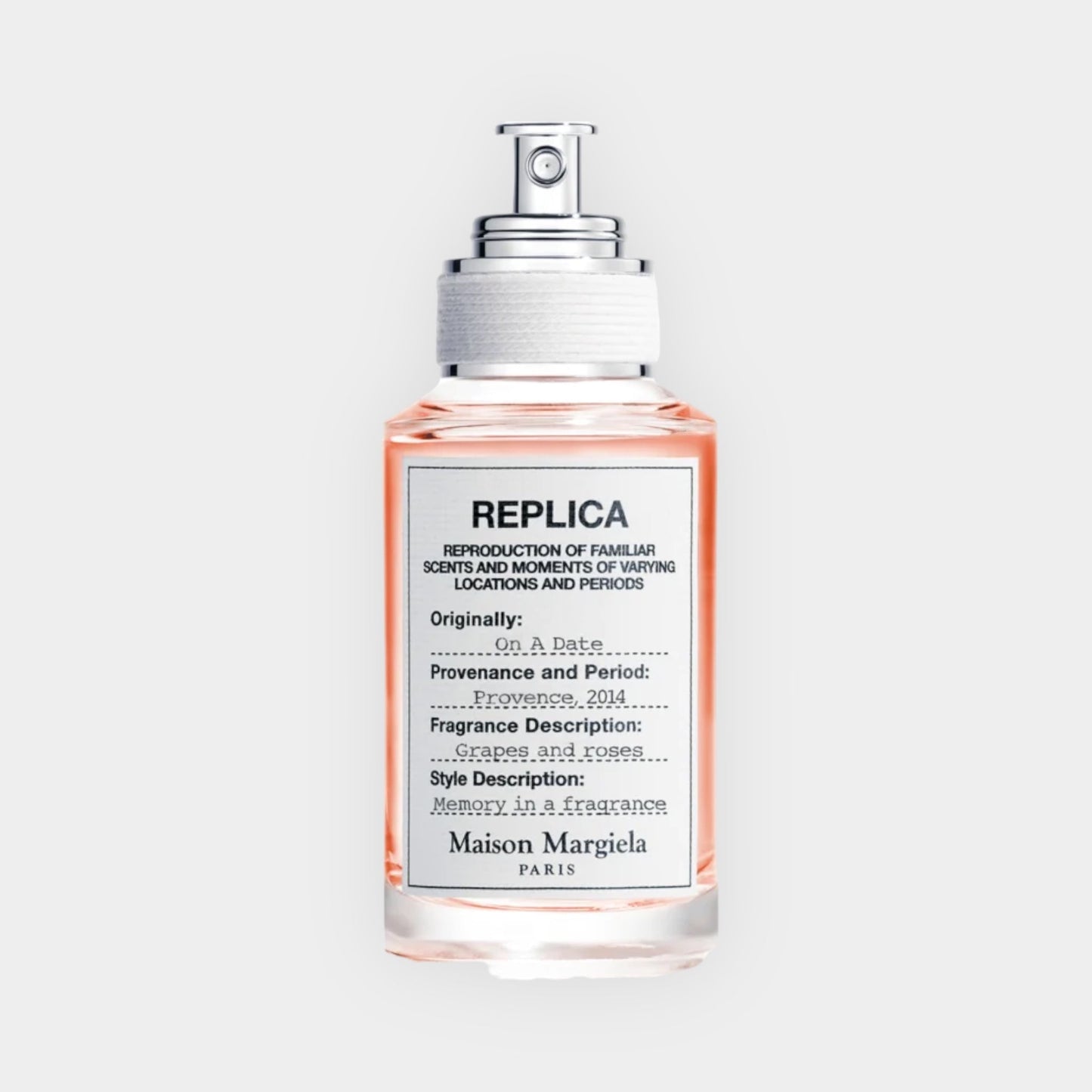 A glass spray bottle of Maison Margiela Replica On a Date Sample, featuring a label that highlights its fragrance description of grapes and roses, paired with a soft pink liquid.
