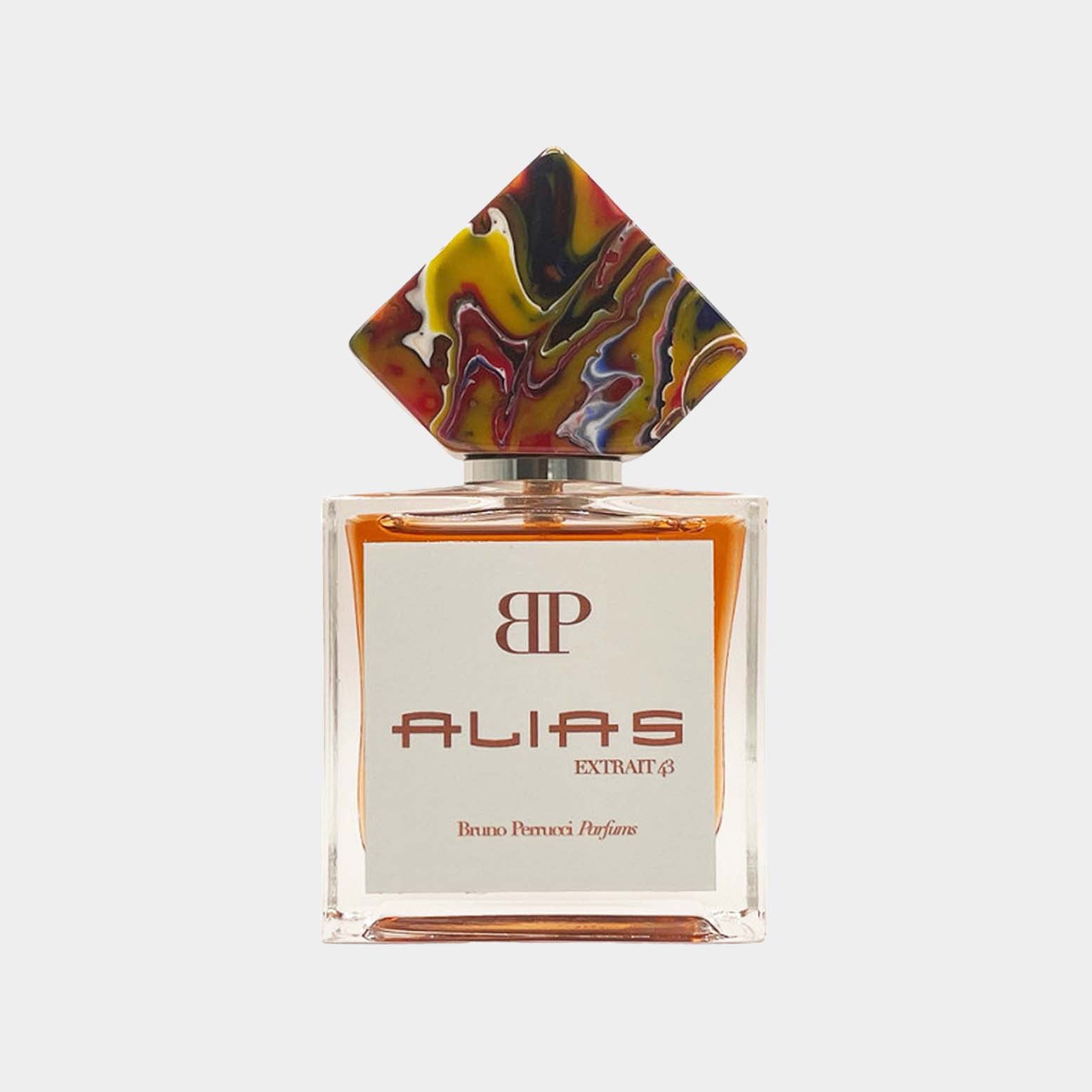 A beautifully designed bottle of Bruno Perrucci Alias Sample perfume featuring a colorful, artistic cap and a clear glass base with a white label displaying the brand name and fragrance title.