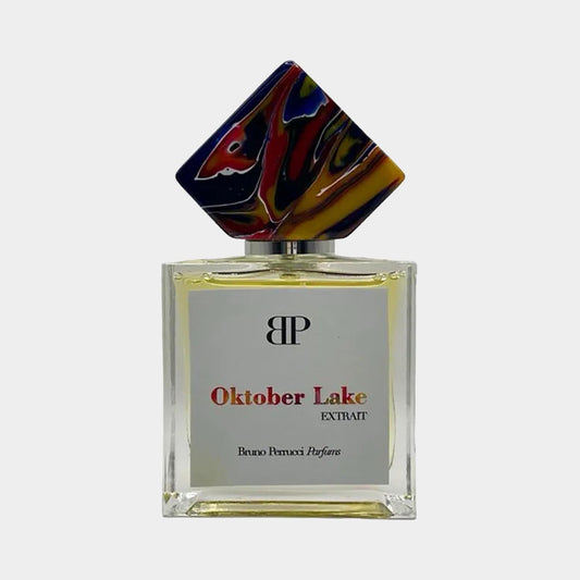 A bottle of Bruno Perrucci Oktober Lake Sample, featuring a vibrant, artistic cap in multiple colors and a sleek rectangular design. The label prominently displays the fragrance name and EXTRAIT.
