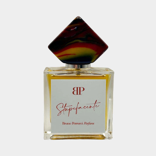 A full bottle of Bruno Perrucci Stupefacente perfume, featuring a square glass base and a uniquely shaped cap with vibrant colors. The elegant label displays the brand name and fragrance title.