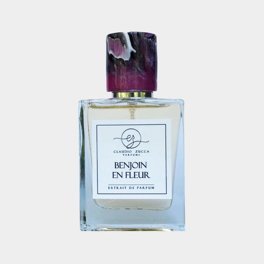 A clear glass perfume bottle with a decorative top, showcasing 'Claudio Zucca Benjoin en Fleur Sample', an extrait de parfum. The label features elegant typography highlighting the fragrance name.
