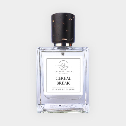 A glass bottle of 'Claudio Zucca Cereal Break Sample' perfume, featuring a sleek design and a black cap with a textured finish. The label displays the name and notes of this extrait de parfum.
