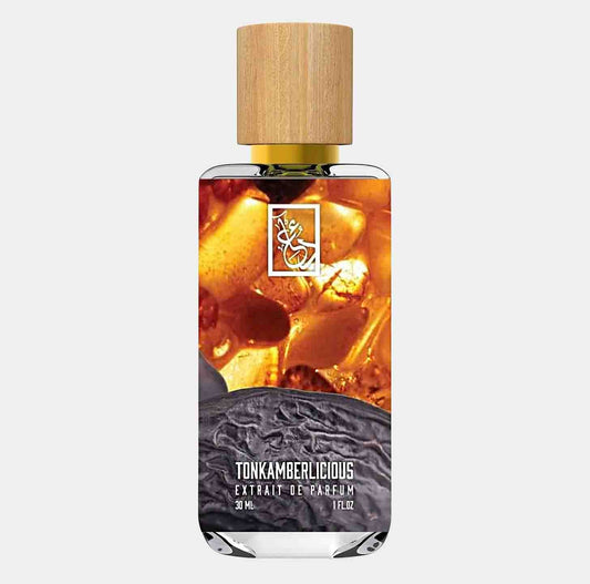A bottle of Dua Tonkamberlicious Sample, featuring a sleek design with a wooden cap and rich, amber-colored liquid, set against a textured background. The label showcases the product name elegantly.
