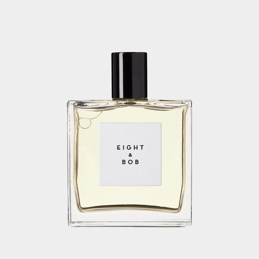 A clear glass bottle of Eight and Bob The Original perfume, featuring a minimalist design with a squared label displaying the brand name in elegant typography. The liquid inside is pale yellow, emphasizing its sophisticated fragrance.