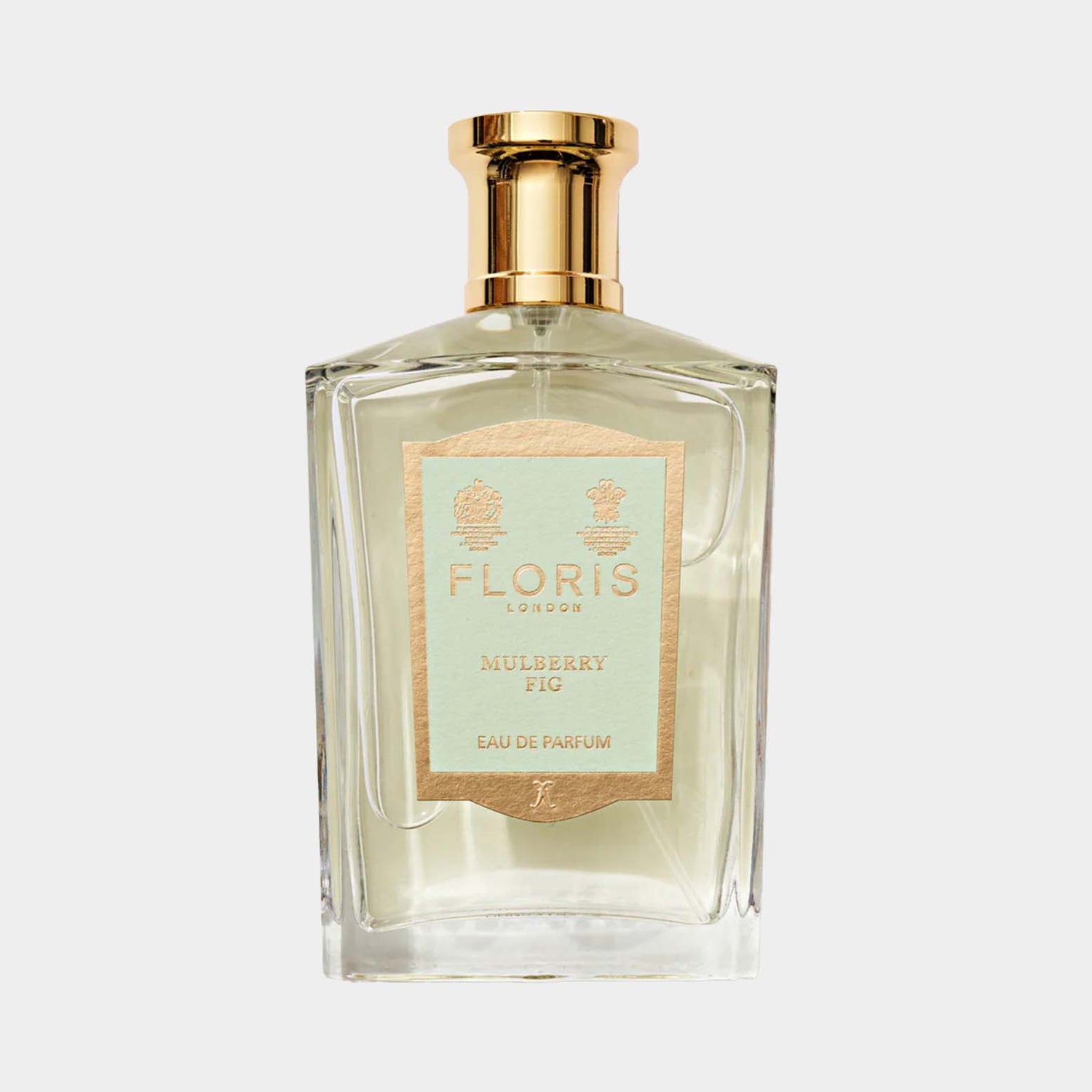 A clear glass bottle of Floris London Mulberry Fig Eau de Parfum, featuring a gold cap and a decorative label with a light blue and gold design. The fragrance encapsulates a blend of mulberry and fig notes.