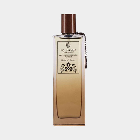 A sleek, rectangular bottle of Galimard Gaiac Precieux Collection Privée sample, featuring a wooden cap and an elegant label with intricate detailing. The fragrance inside has a warm, amber hue.