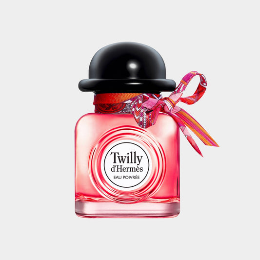 A small bottle of Hermès Twilly d'Hermès Eau Poivrée EDP, featuring a vibrant pink liquid, a black hat-like cap, and a colorful ribbon tied around the neck. The elegant packaging showcases the brand's signature style.