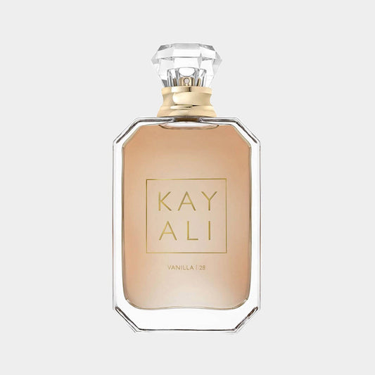 A clear glass bottle of Kayali Vanilla 28 Sample, featuring a geometric design and a diamond-shaped cap, showcasing a warm beige fragrance inside.