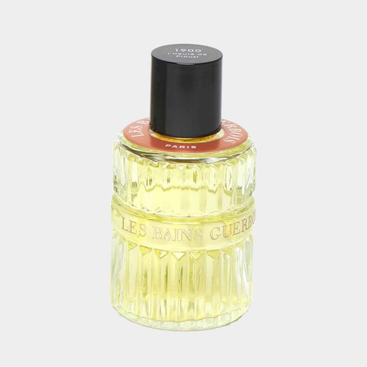 A glass bottle of Les Bains Guerbois L'Heure de Proust 1900 sample perfume, featuring a textured design and a black cap, set against a light background.