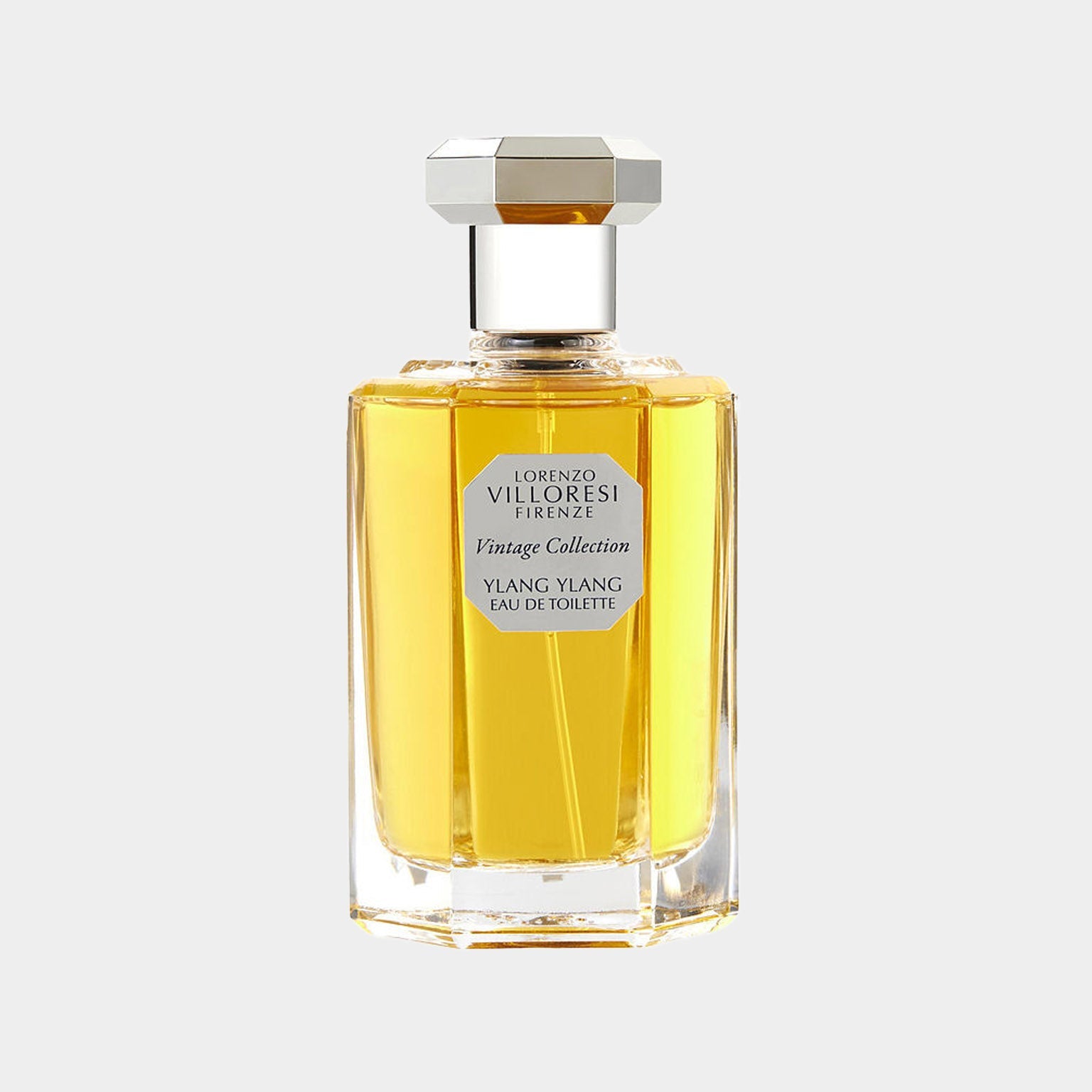 A bottle of Lorenzo Villoresi Ylang Ylang Eau de Toilette, featuring a sleek, transparent design with a hexagonal cap, filled with a vibrant yellow liquid. The label highlights its inclusion in the Vintage Collection.