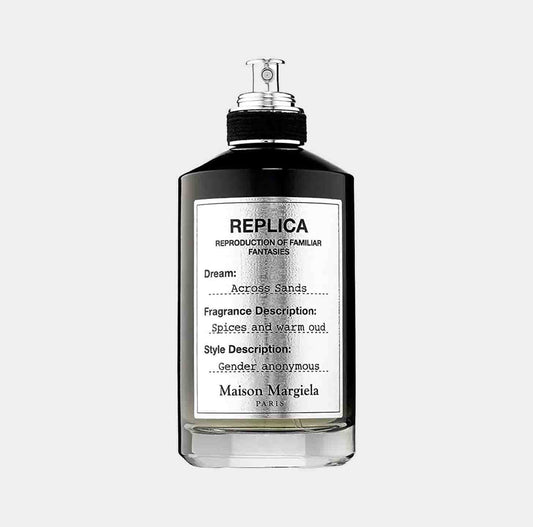 A sleek bottle of Maison Martin Margiela Replica Across Sands Sample, featuring a minimalist design with a black cap and a label that describes the fragrance as a blend of spices and warm oud. The bottle embodies a gender-neutral aesthetic.