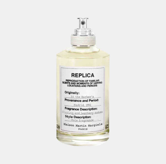 A bottle of Maison Martin Margiela Replica At the Barber's Sample fragrance, featuring a clear glass design and a label detailing the scent's provenance, fragrance descriptors, and style description.