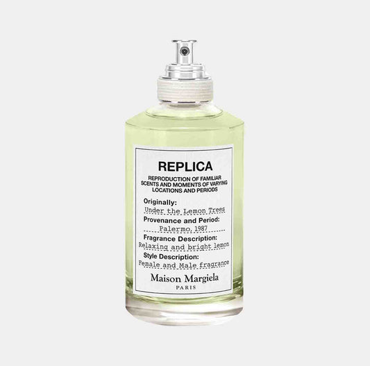 A glass bottle of Maison Martin Margiela Replica Under the Lemon Trees Sample, featuring a light green liquid inside and a minimalist label that describes its origins and fragrance notes of relaxing lemon and male fragrance.