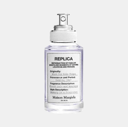 A clear bottle of Maison Martin Margiela Replica When the Rain Stops Sample, featuring a minimalist design and a pump spray cap. The label indicates its origin from Dublin, 1967, with a fragrance description of fresh and subtle scents.