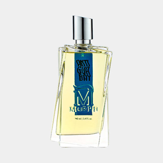 A full bottle of Morph Antigua Bay, featuring a uniquely shaped glass design with a silver cap and a blue label. The bottle contains a fresh, yellow fragrance and holds 100 ml (3.4 fl. oz).