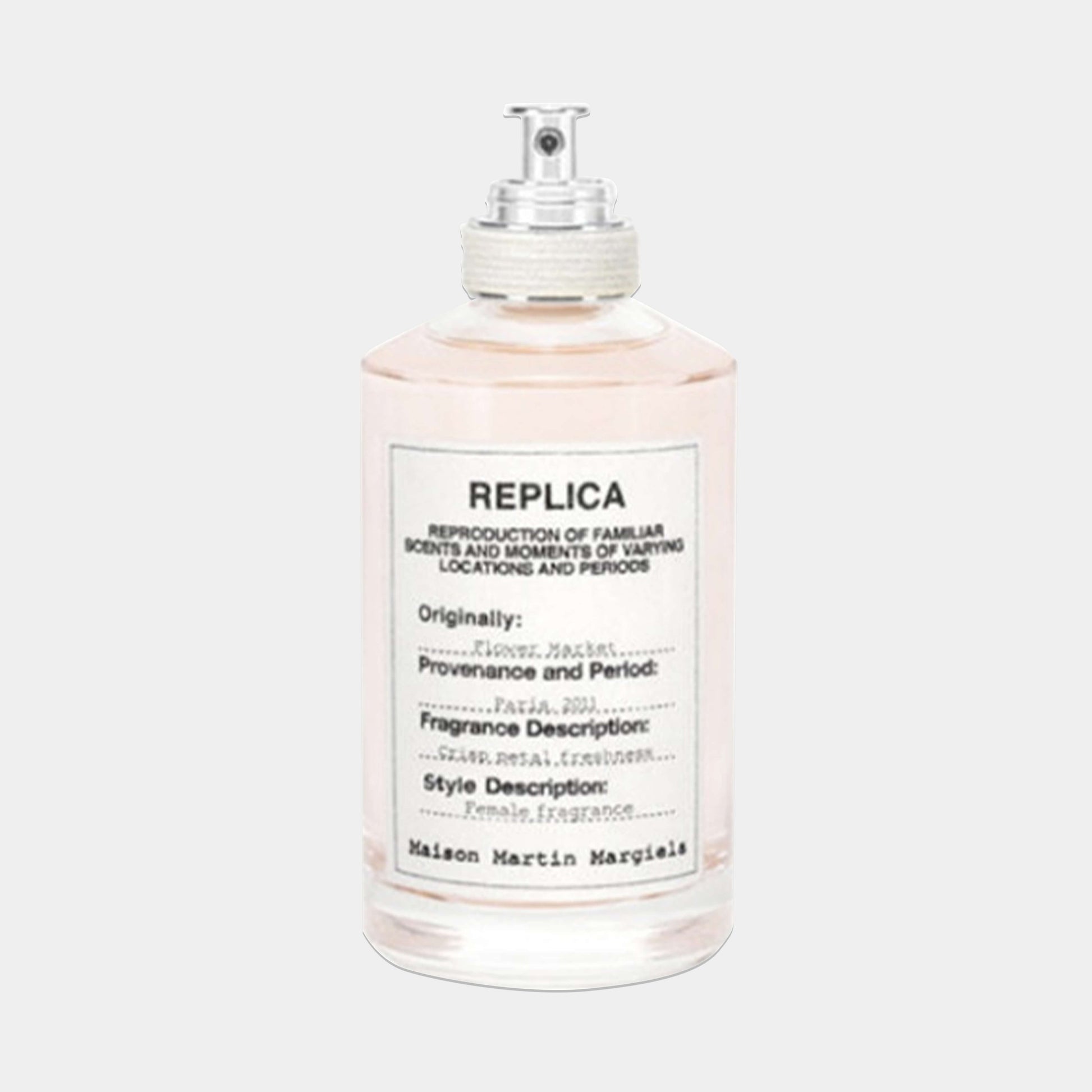 A clear bottle of Maison Martin Margiela Replica Flower Market Sample fragrance, featuring a minimalist design with a silver spray nozzle and a label that describes the scent’s inspiration and profile.