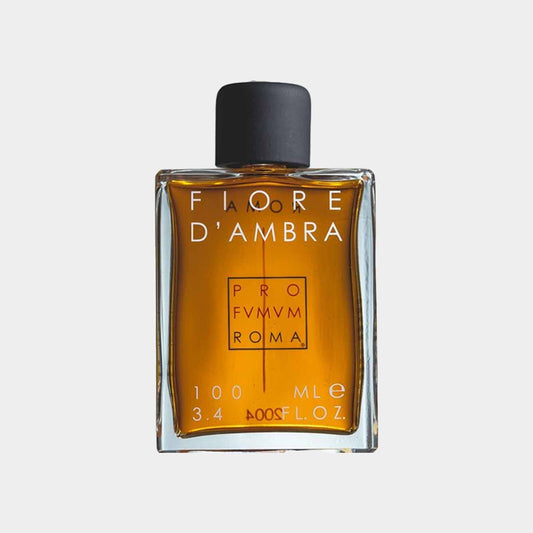 A clear glass bottle of Profumum Roma Fiore D'Ambra fragrance, featuring an elegant design with a black cap and a warm amber liquid inside. The label includes the brand name and product details.