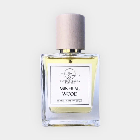 A clear glass bottle of Claudio Zucca Mineral Wood Sample perfume, featuring a wooden cap and a label that reads MINERAL WOOD EXTRAIT DE PARFUM in elegant font. The liquid inside is a pale yellow hue.