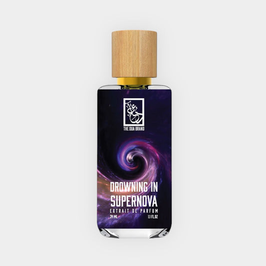 A stylish bottle of Dua Drowning in Supernova perfume, featuring a swirling cosmic design on the label and a wooden cap, showcasing its luxurious fragrance essence.
